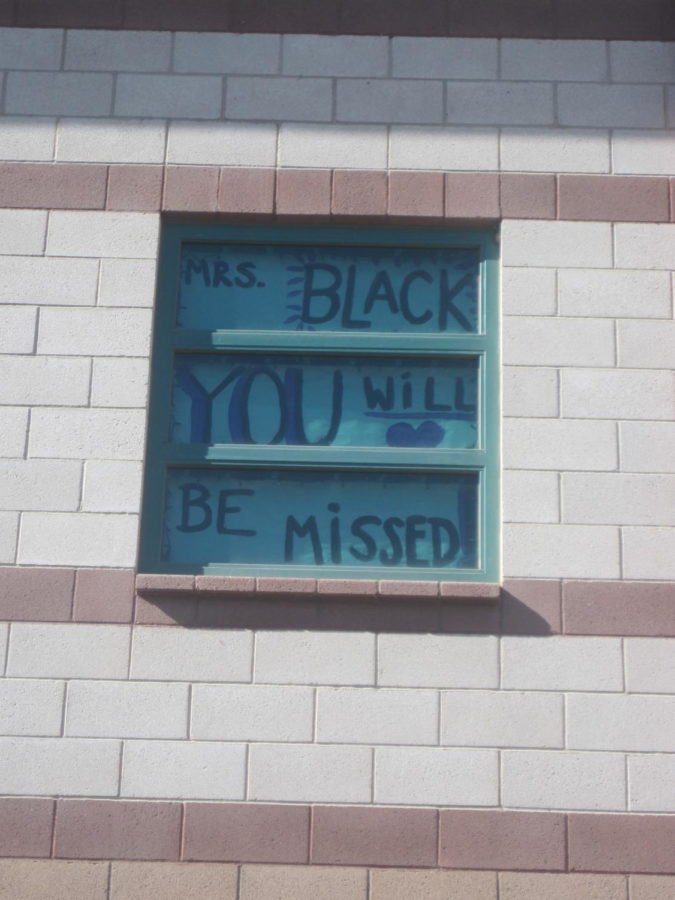 A poster read Mrs. Black, you will be missed sticks out the window of Mrs. Blacks classroom so that people passing by could see it and remember her. 