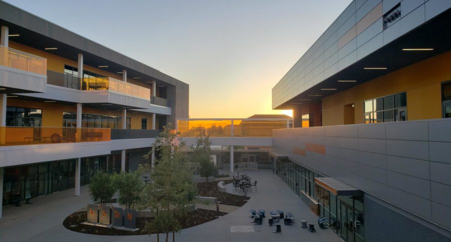 On the steps of the eSTEM building, just beyond the orange bridge wall, the shape of a main campus building can just barely be made out, with the morning sun rising behind.